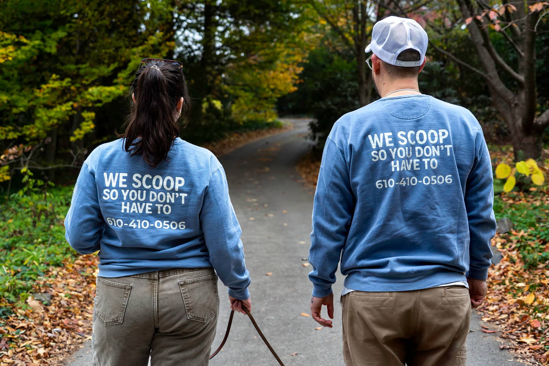 Two staff walking away up a path, sweatshirts printed “We scoop so you don't have to”