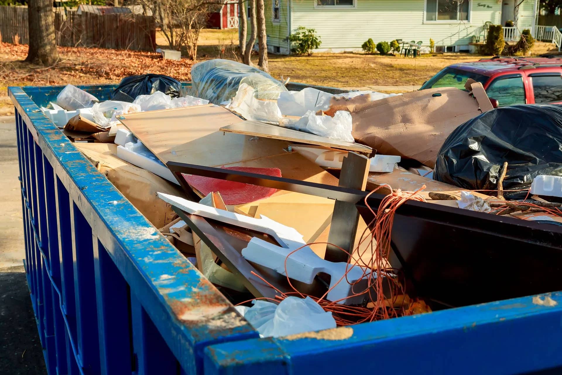 A blue skip on a driveway, filled with household junk and bagged waste